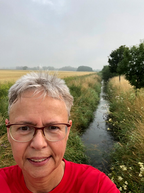 Muko-Spendenlauf 2021 - Selfie von Ursula, in Hintergund Felder und ein kleiner Wassergraben