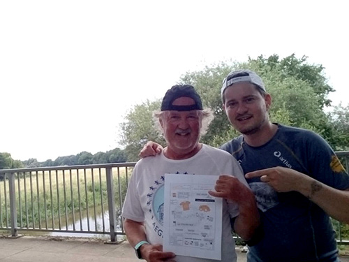 Muko-Spendenlauf 2021 - Wilfried und Dominik stehtn auf einer Brücke und zeigen dabei die Sketchnote zum Muko-Spendenlauf