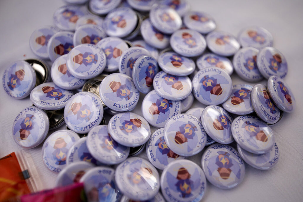 Foto vom 17. Muko-Spendenlauf 2024: viele Buttons auf einem Tisch, auf den Buttons ist eine Zeichnung und "Schutzengel 2024"