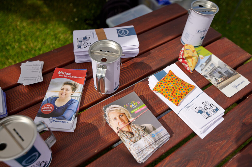 Foto vom 17. Muko-Spendenlauf 2024: Infomaterial, Spendendosen auf einem Holztisch