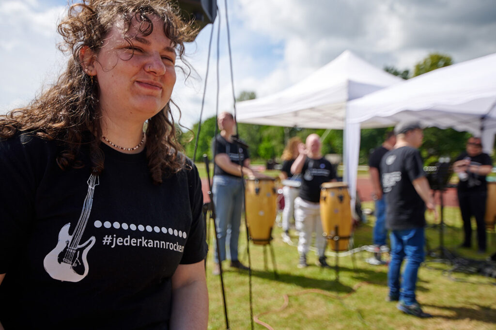 Foto vom 17. Muko-Spendenlauf 2024: Die Hand Hand in Hand, eine Frau ist im Vordergrund, sie trägt ein schwarzes T-Shirt mit der Aufschrift "#jederkannrocken"